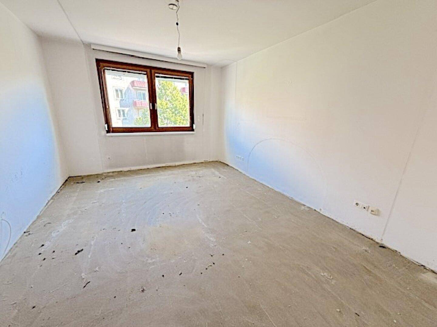 Unmöbliertes Schlafzimmer mit Betonboden und einem Fenster, bereit zur individuellen Gestaltung.