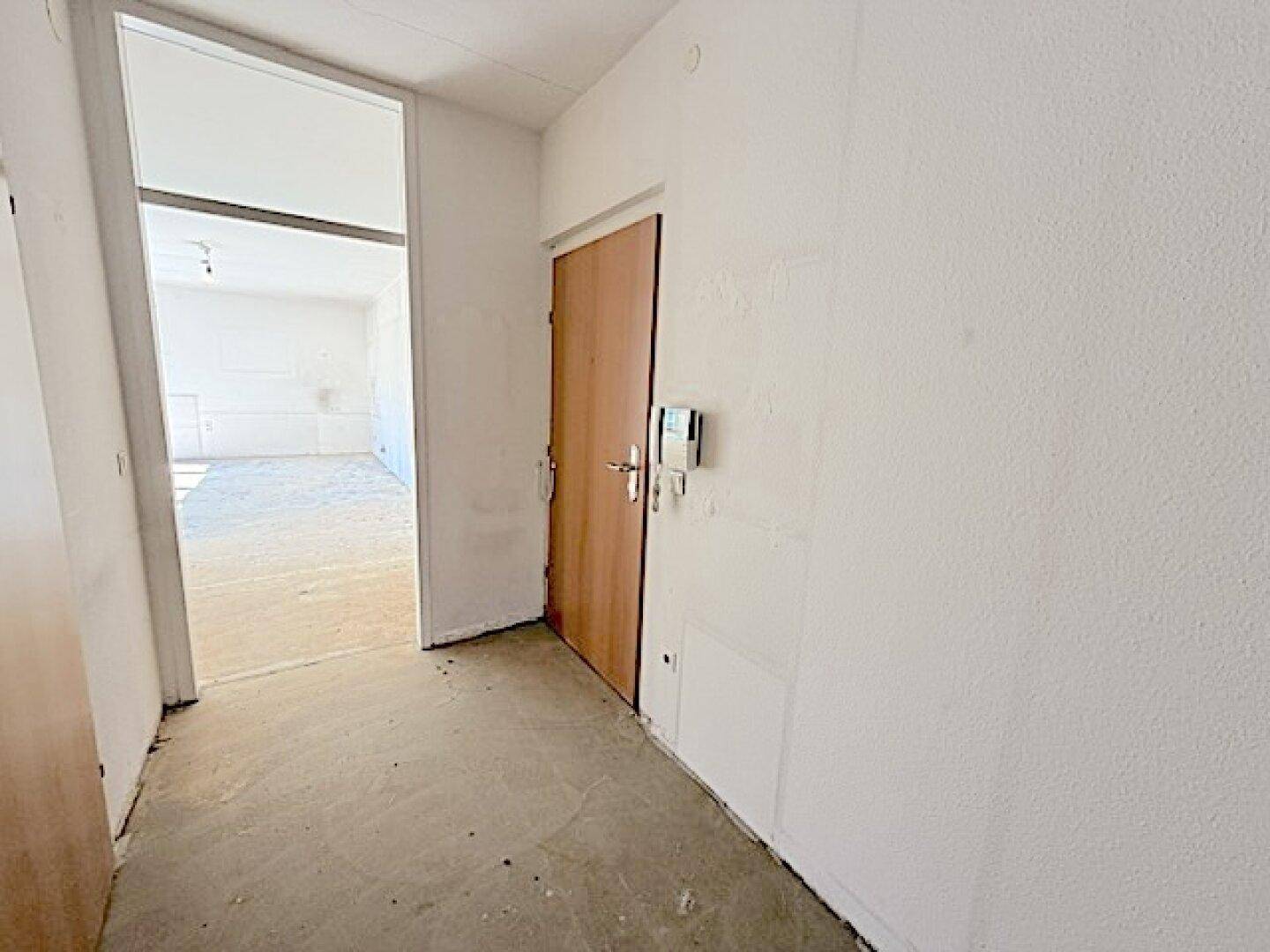 Eingangsbereich mit Betonboden und Holztür, der in die hellen Wohnräume führt.