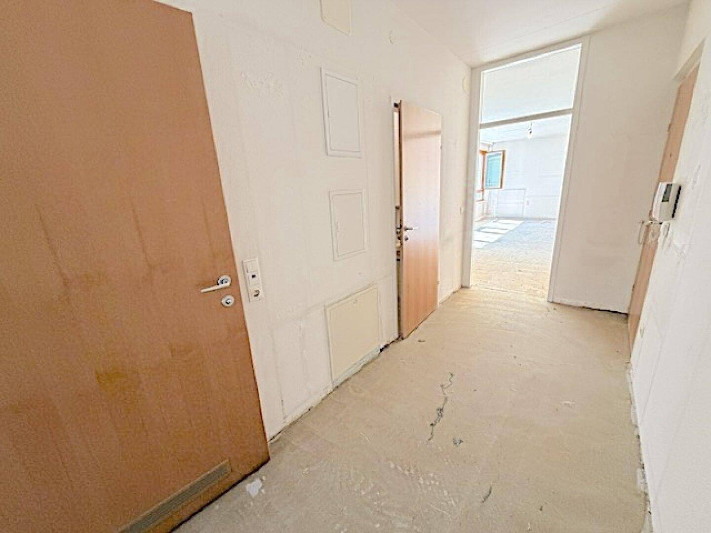Geräumiger Flur mit Betonboden und Holztüren, der einen hellen Übergang zu den Wohnbereichen bietet.