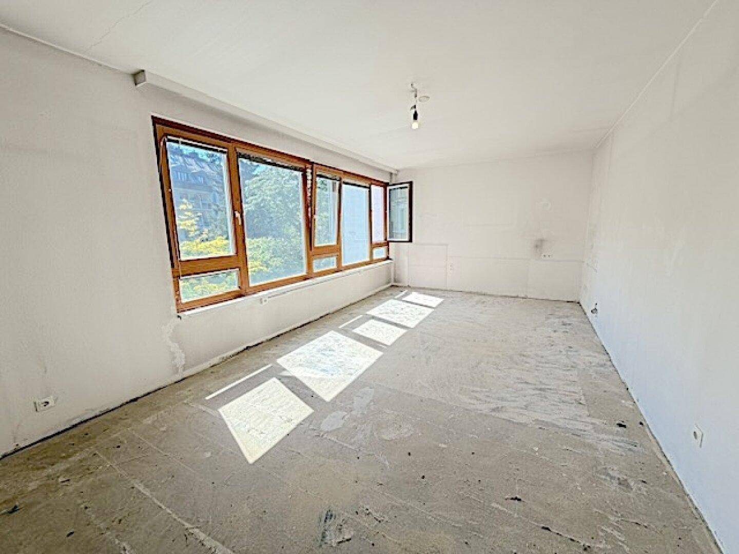 Heller Wohnraum mit großen Fenstern und Betonboden, der viel Potenzial für individuelle Gestaltung bietet.