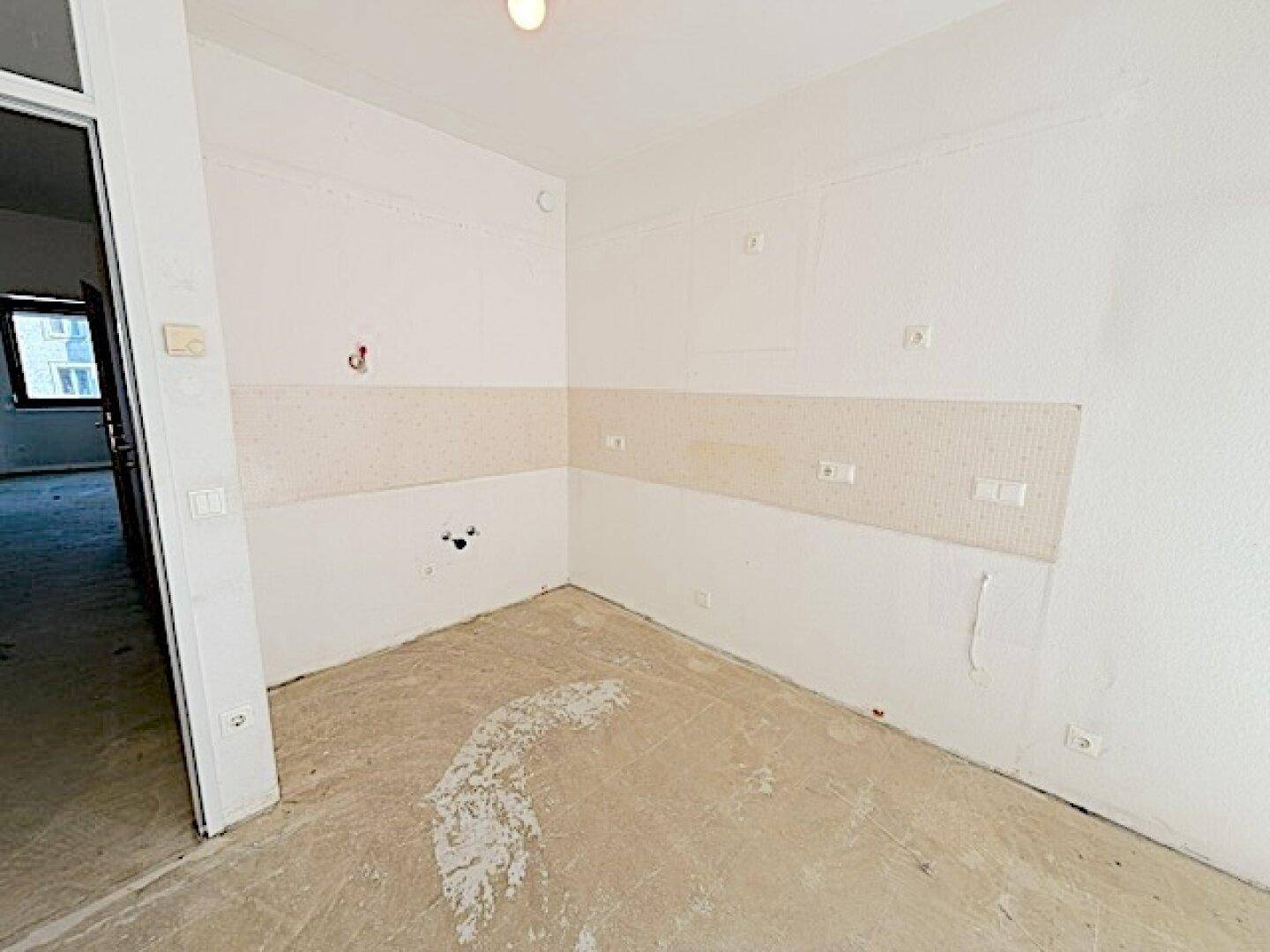Leere Küche mit vorbereiteten Anschlüssen und Betonboden, ideal für eine moderne Einbauküche.