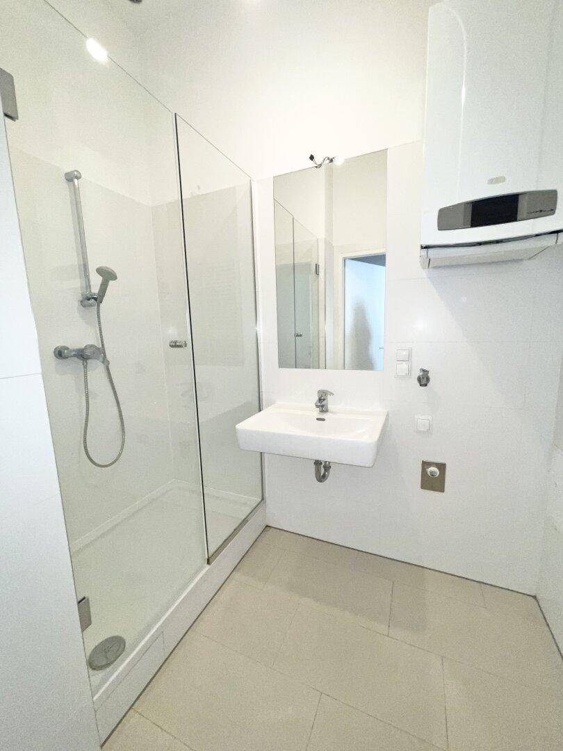 Modernes Badezimmer mit ebenerdiger Dusche, Waschbecken und Spiegel, ausgestattet mit einem Warmwasserbereiter.