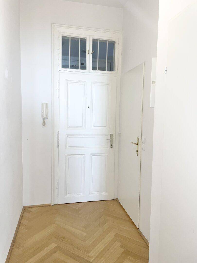 Heller Eingangsbereich mit klassischer weißer Wohnungstür, Gegensprechanlage und Fischgrätparkett.