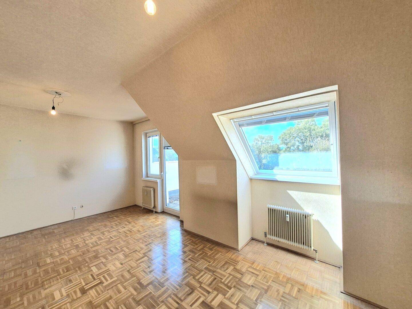 Helles Wohnzimmer mit Dachschräge, Dachfenster und Fischgrätparkettboden.