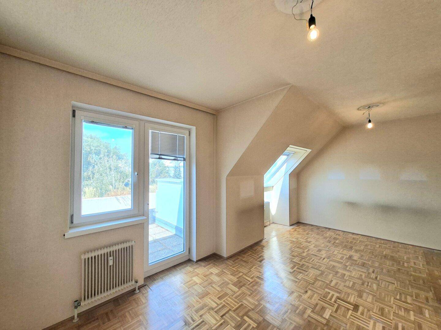 Heller Wohnraum mit Parkettboden, Zugang zu einem Außenbereich und Dachschräge.