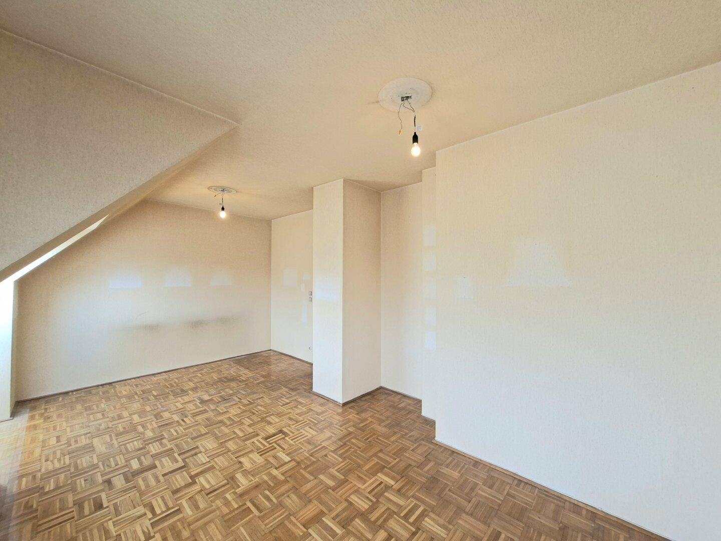 Großer, heller Raum mit Parkettboden und charakteristischer Dachschräge.