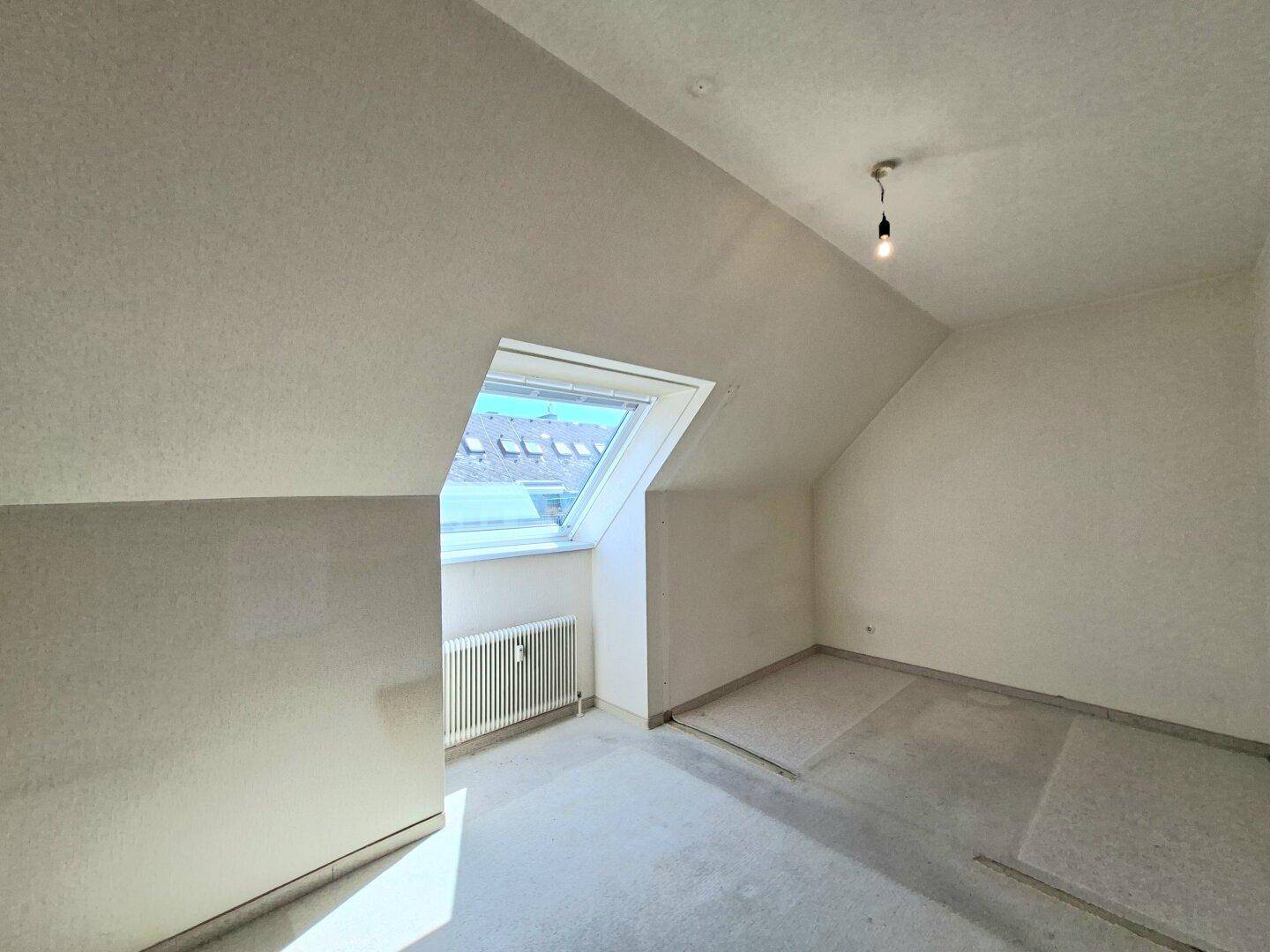 Helles Schlafzimmer mit Dachschräge, Dachfenster und vorbereitetem Bodenbelag.