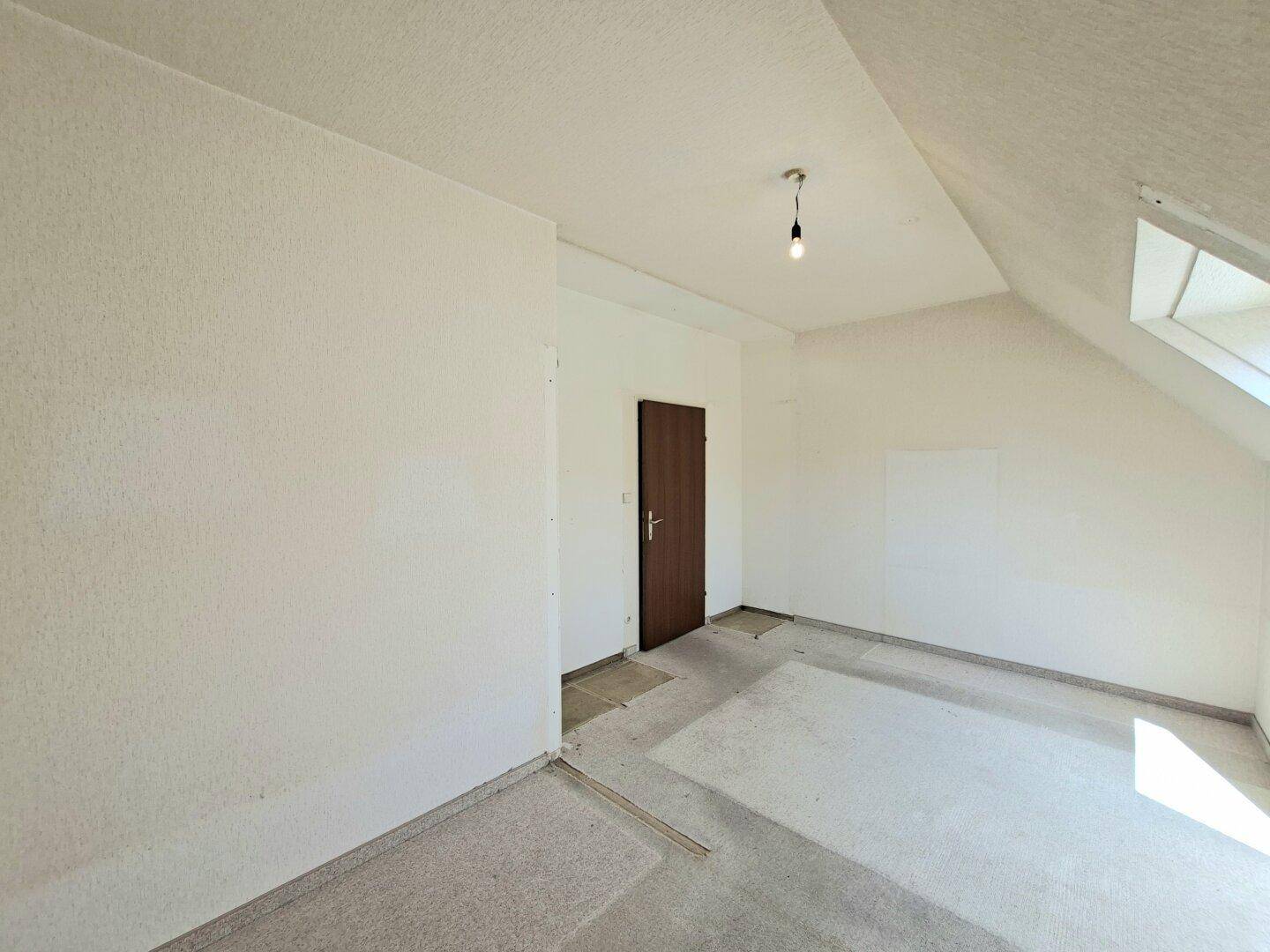 Geräumiges Schlafzimmer mit Dachschräge, Holztür und unfertigem Bodenbelag.