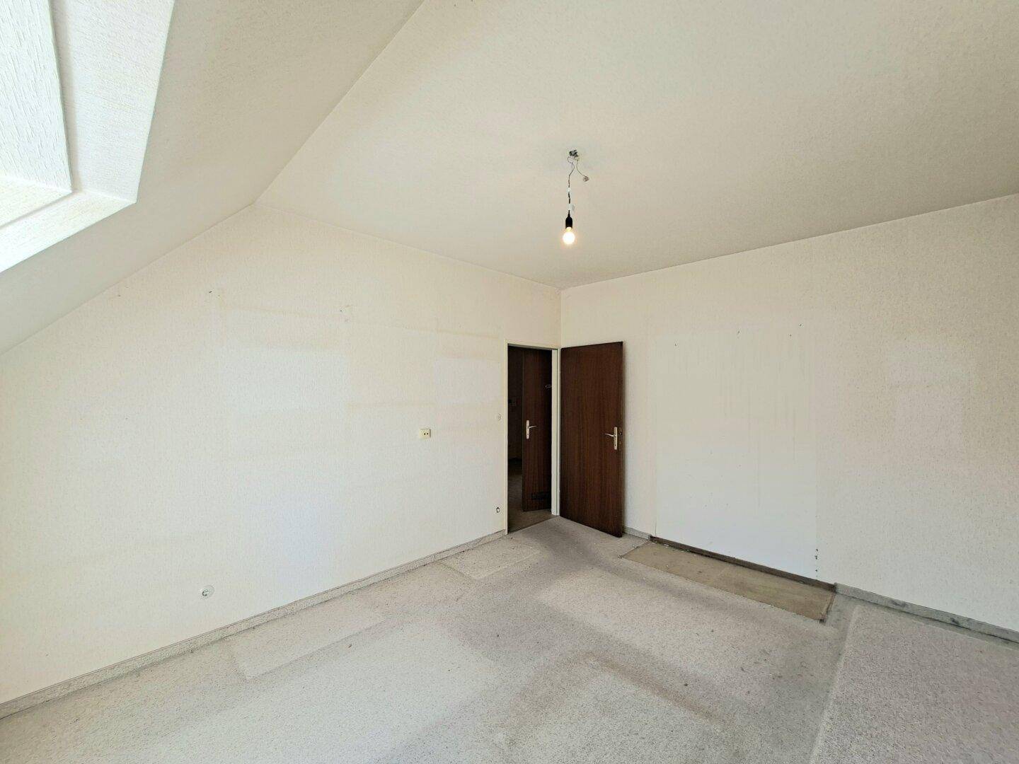 Helles Schlafzimmer mit Dachschräge, zwei Türen und unfertigem Bodenbelag.