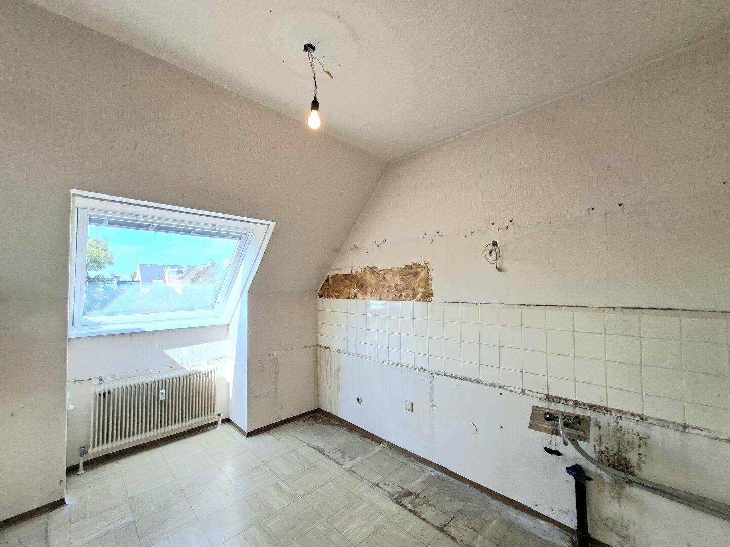 Küche mit Dachschräge, Dachfenster und alten Wandfliesen, bereit zur Renovierung.