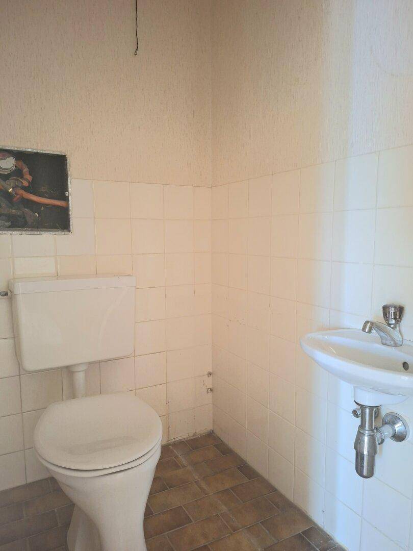 Separates WC mit Toilette, kleinem Waschbecken und weißen Wandfliesen.