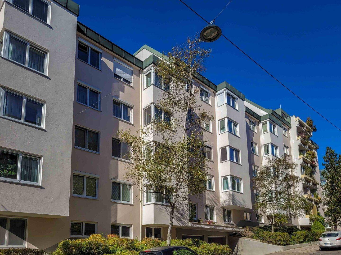 Mehrstöckiges Wohngebäude mit mehreren Balkonen und grüner Umgebung unter blauem Himmel.