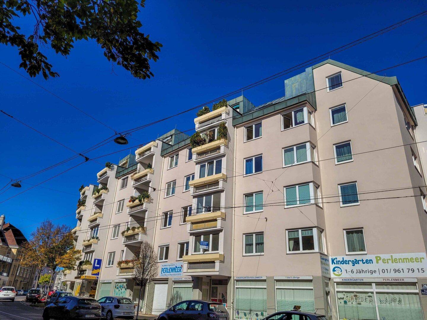 Mehrstöckiges Wohn- und Geschäftsgebäude mit Balkonen und Geschäften im Erdgeschoss an einer Straße.