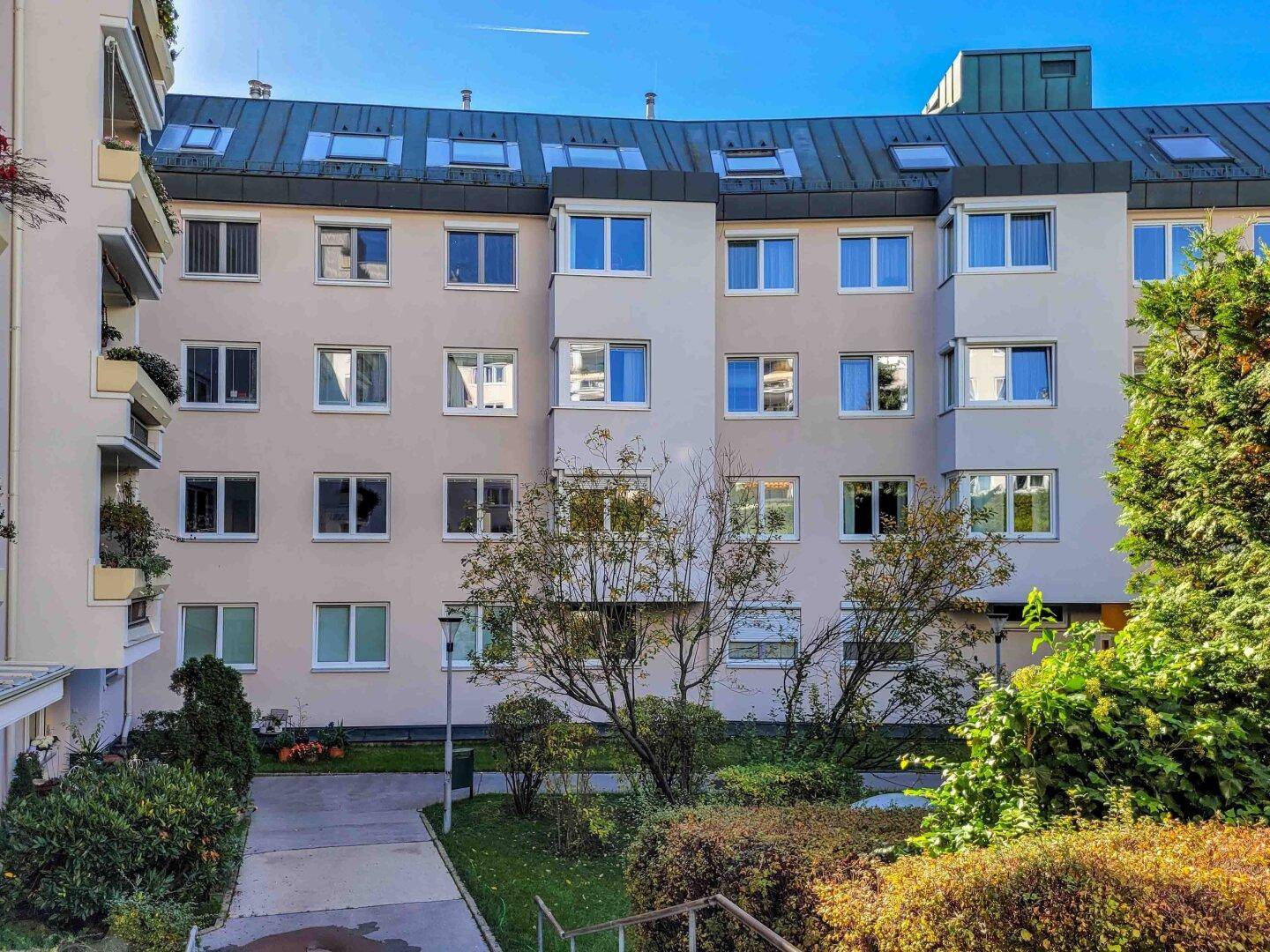 Gepflegter Innenhof eines Wohnkomplexes mit Grünflächen, Bäumen und einem Gehweg.