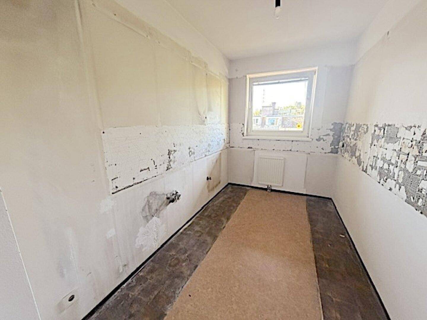 Leere Küche in Renovierung mit Fenster und vorbereiteten Wänden.