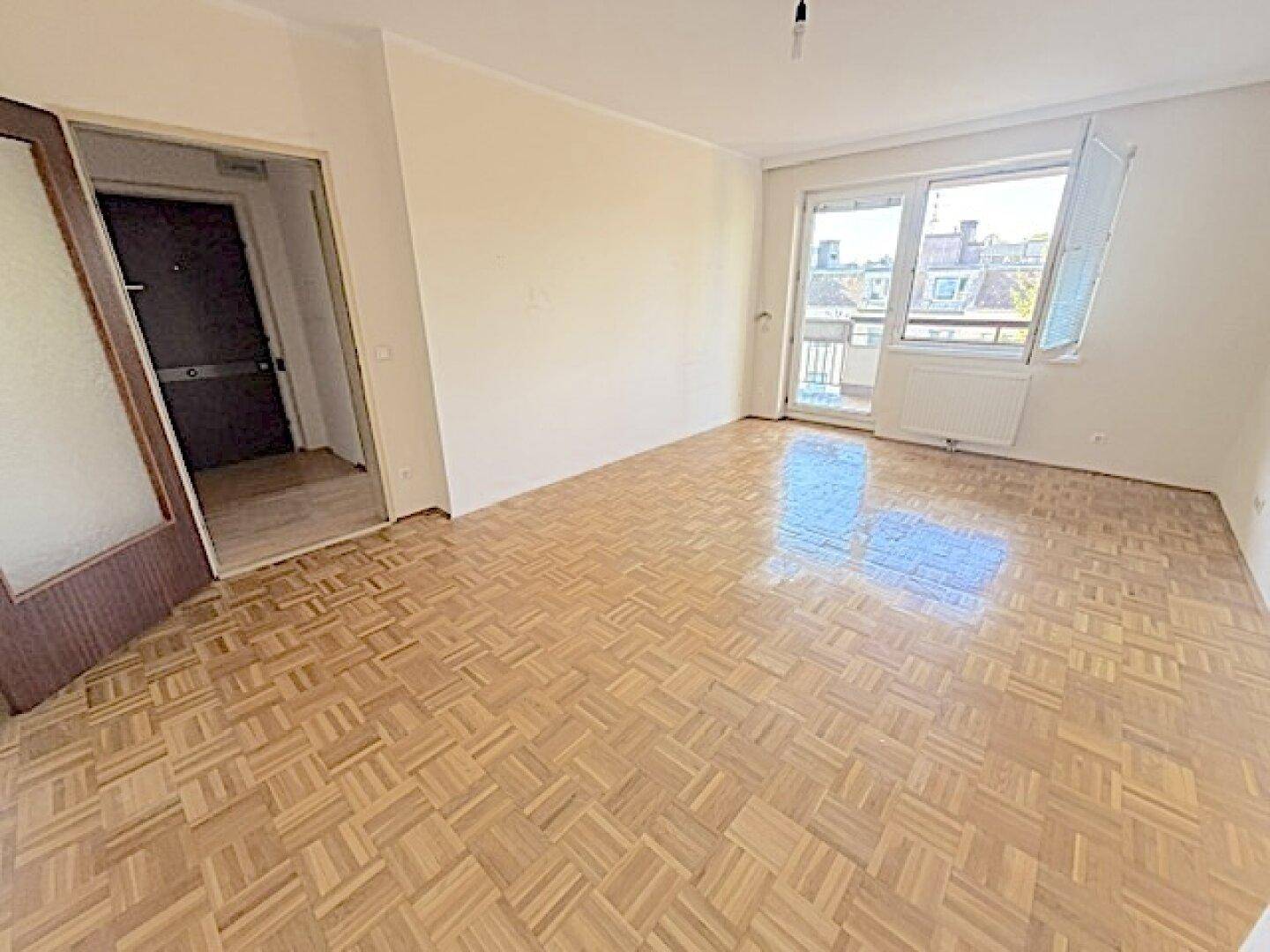 Geräumiges, helles Zimmer mit Parkettboden und Zugang zum Balkon.