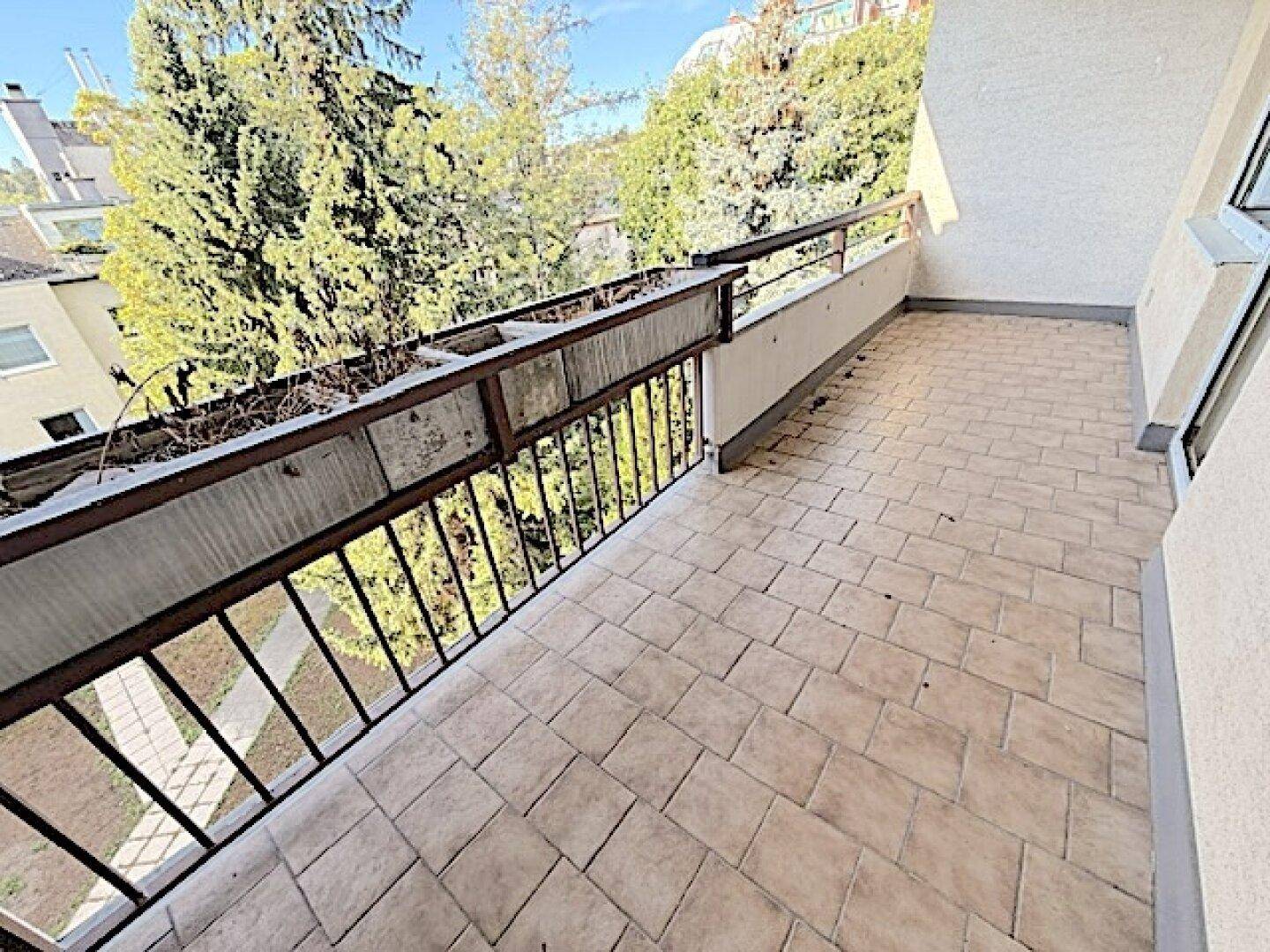 Langer Balkon mit Fliesenboden und Blick auf grüne Bäume.