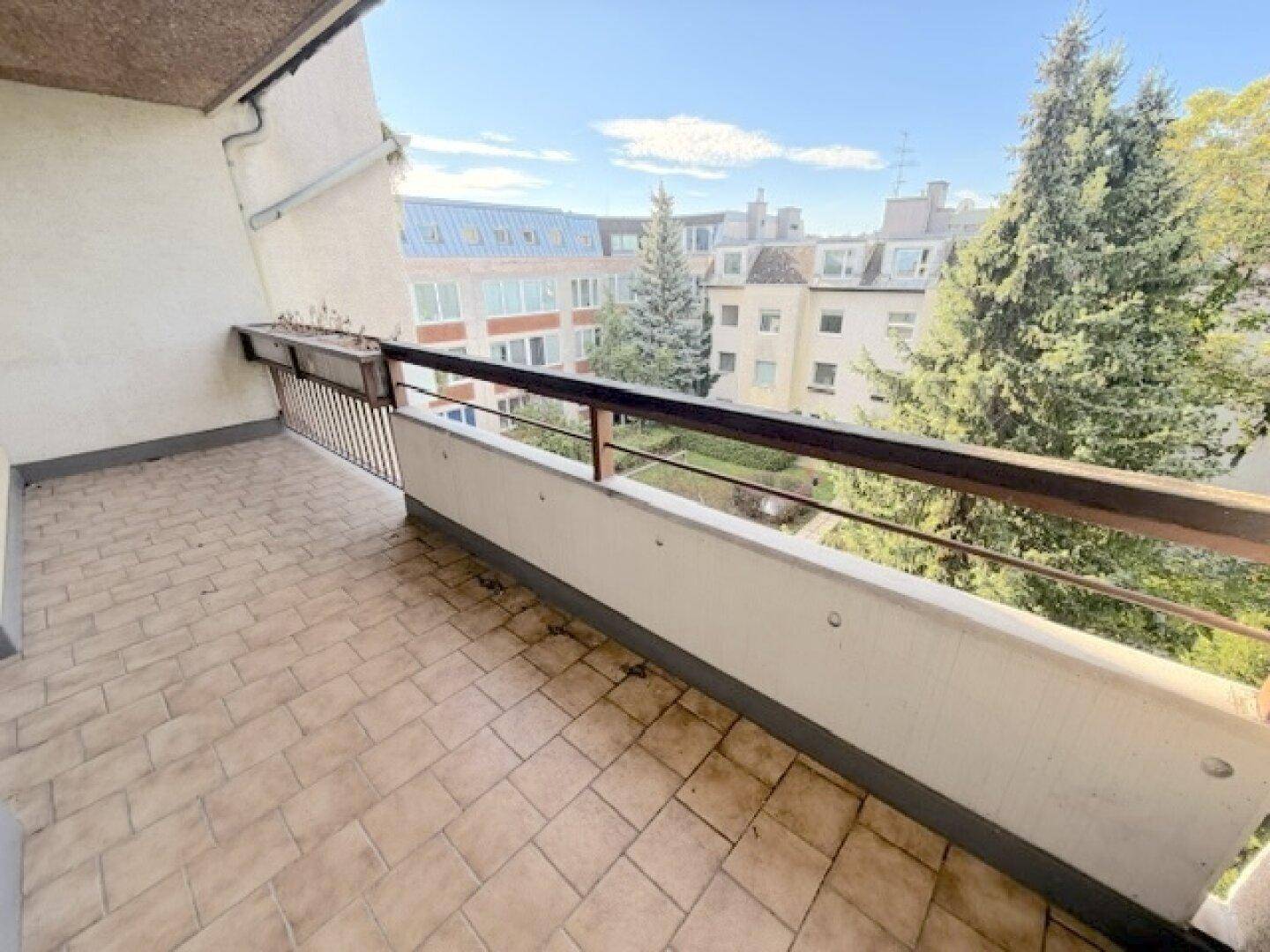 Balkon mit Fliesenboden und Blick auf die umliegenden Gebäude und Bäume.
