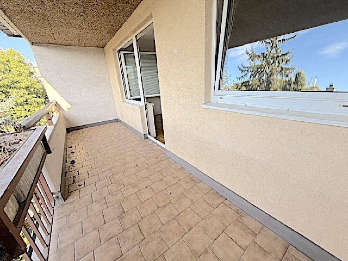 Balkon mit Fliesenboden und Zugang zu einem Innenraum, umgeben von Bäumen.