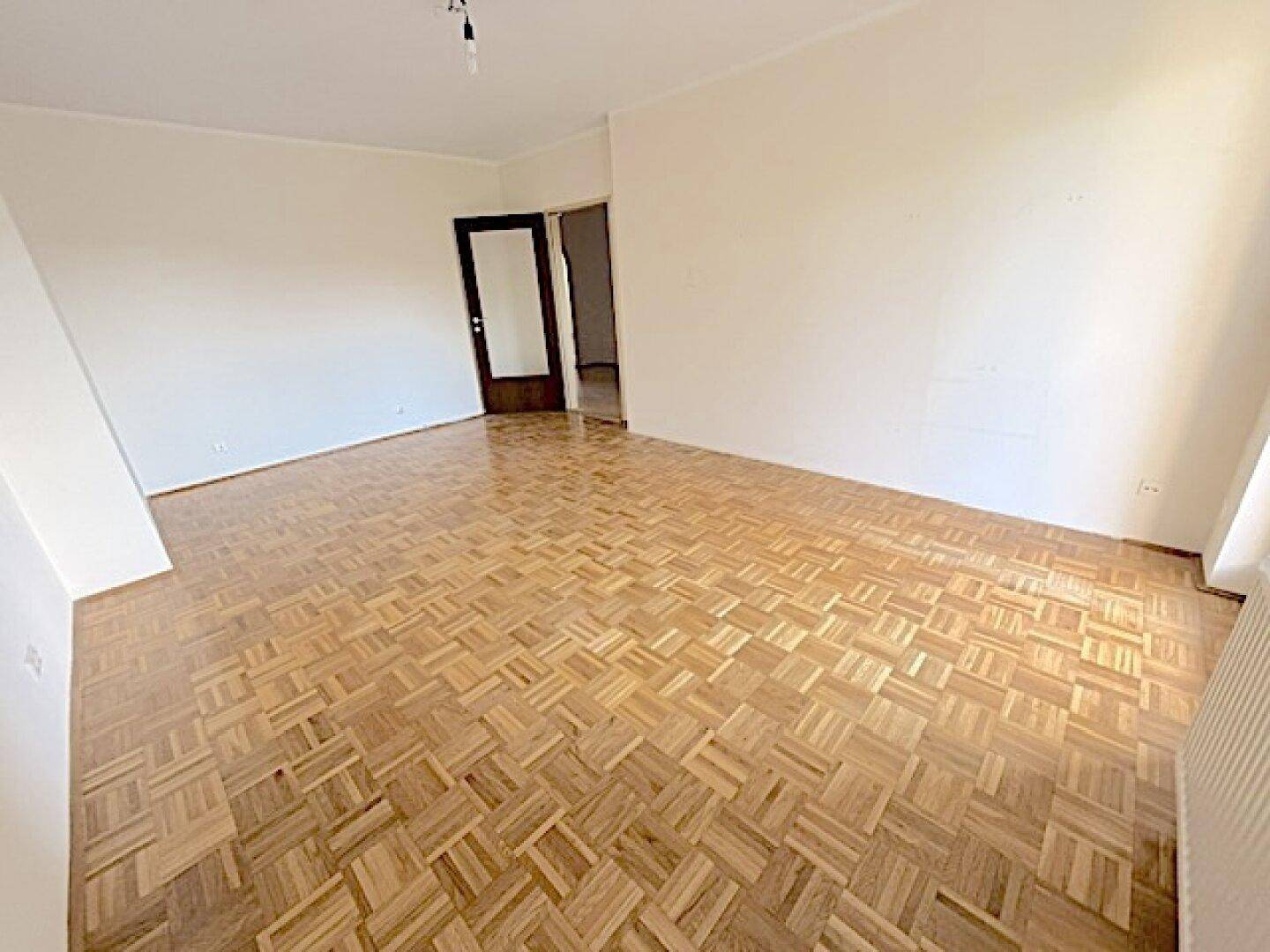 Leeres Zimmer mit Parkettboden und weiß gestrichenen Wänden.