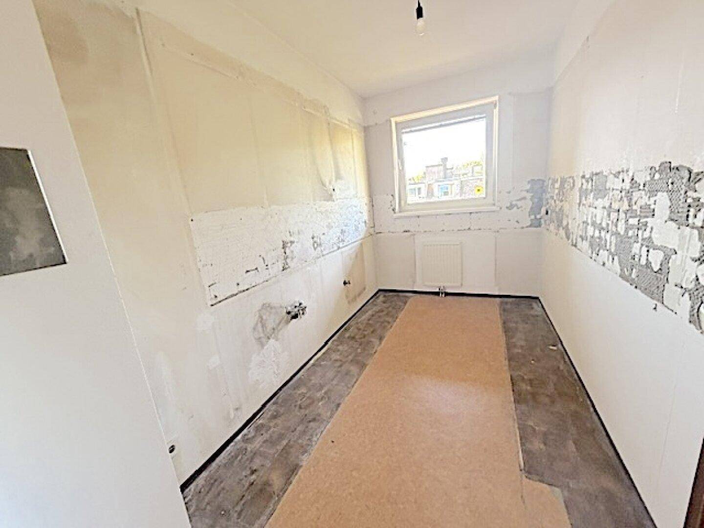 Leere Küche in Renovierung mit Fenster und vorbereiteten Wänden.