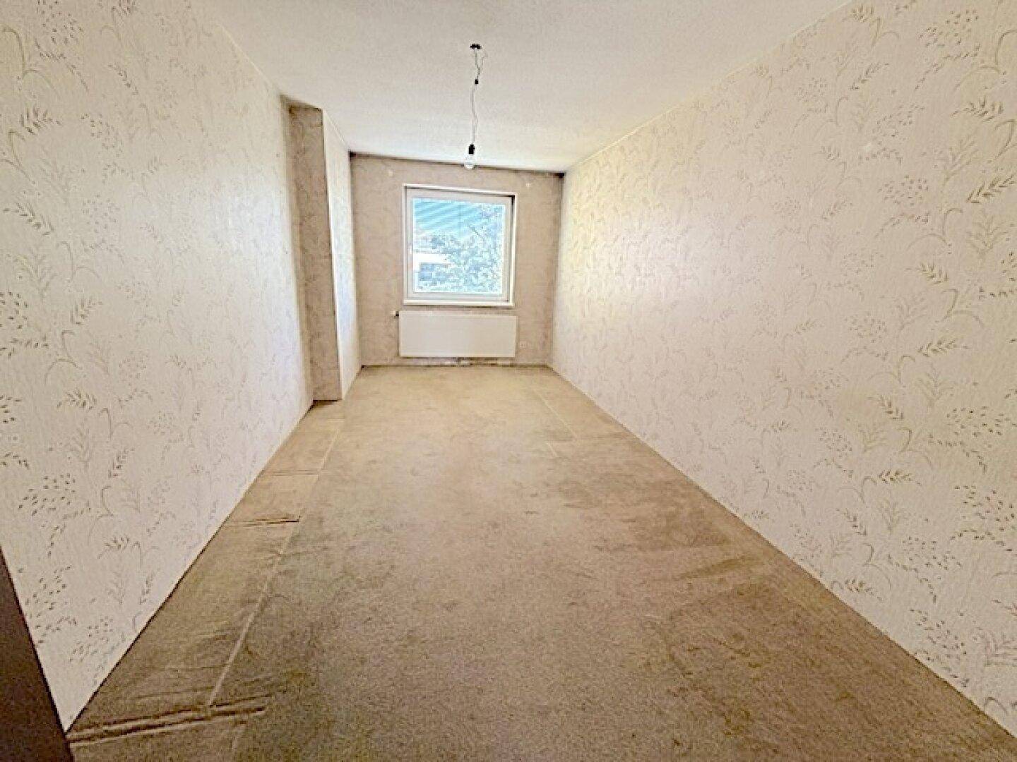 Leeres Zimmer mit gemusterter Tapete und Fenster, bereit zur individuellen Gestaltung.