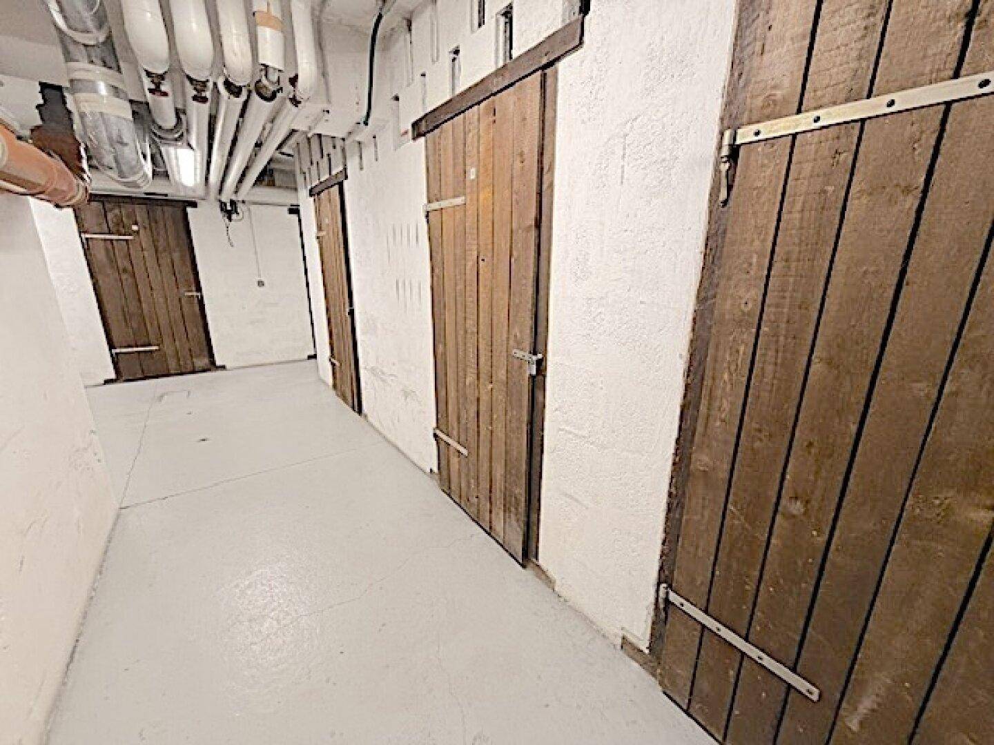 Reihe von Holzverschlägen im Kellerbereich, die als private Abstellräume dienen.