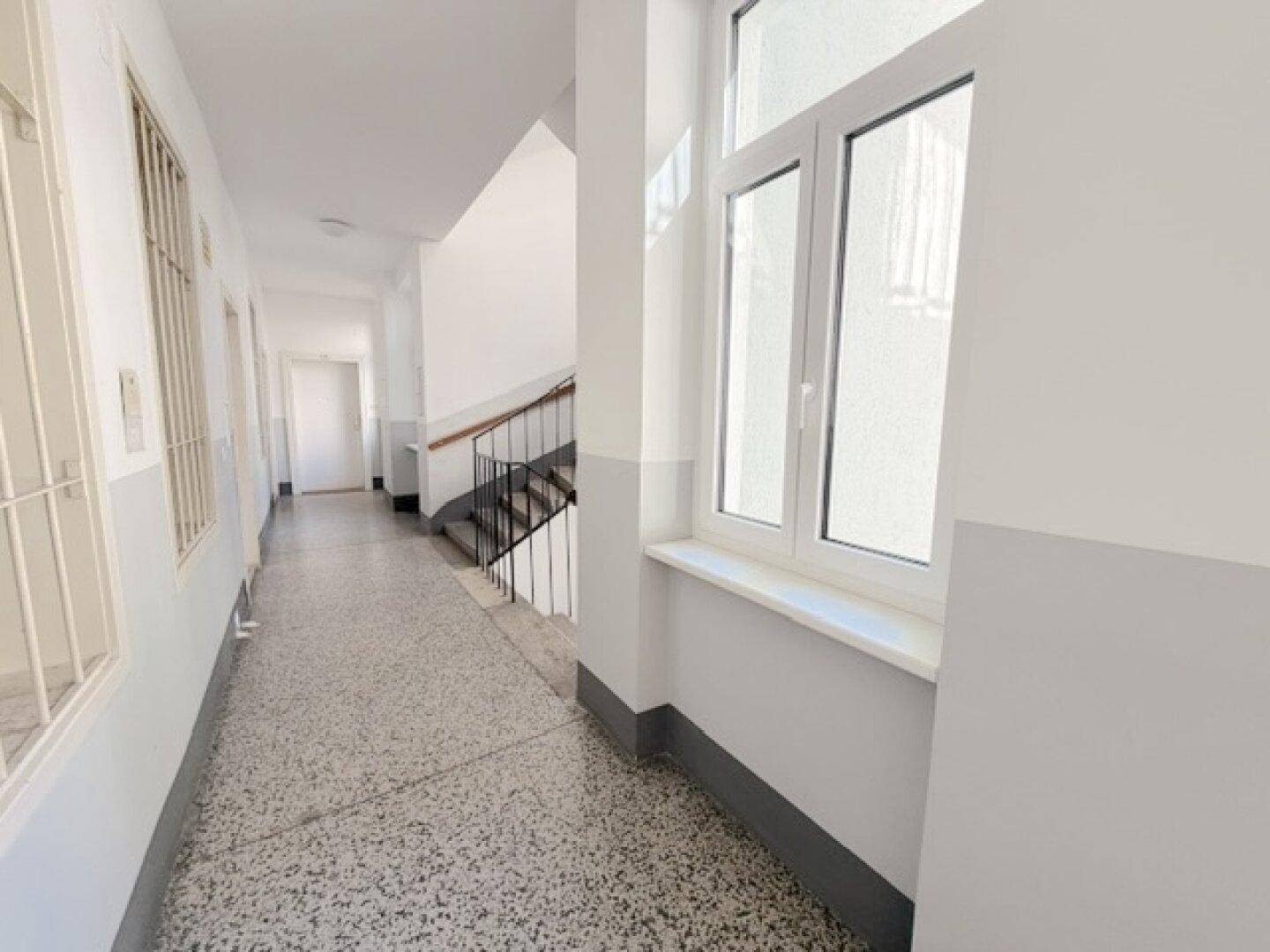 Heller Hausflur mit Terrazzoboden und Treppenaufgang in einem Altbau.