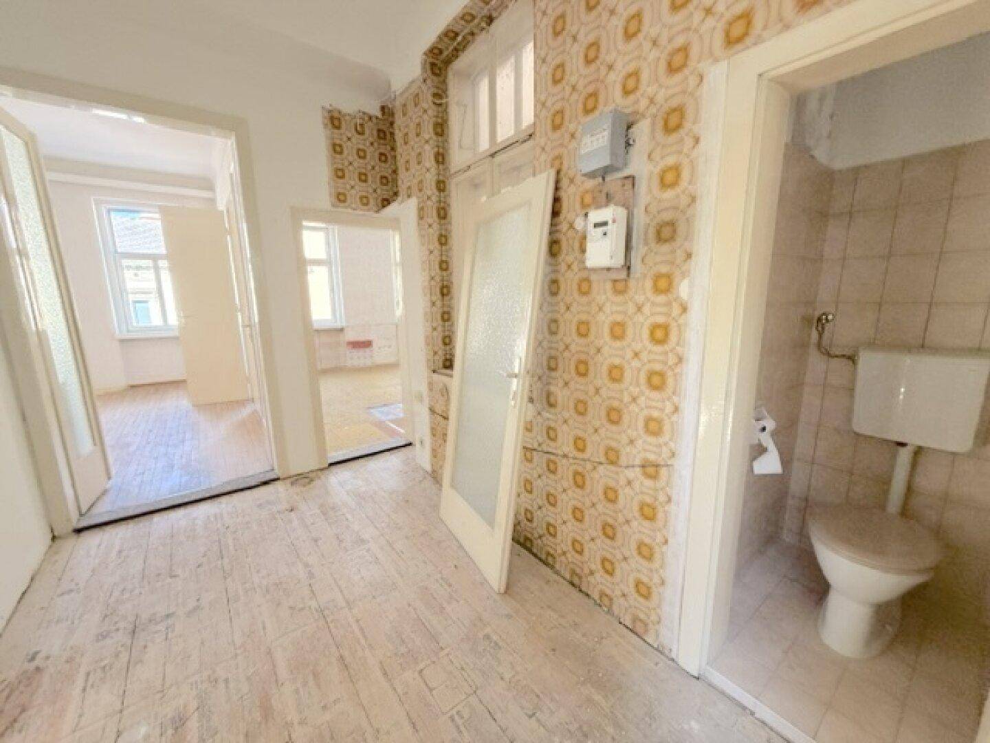 Flur mit auffälliger Tapete, Holzboden und Zugang zu verschiedenen Zimmern und WC.