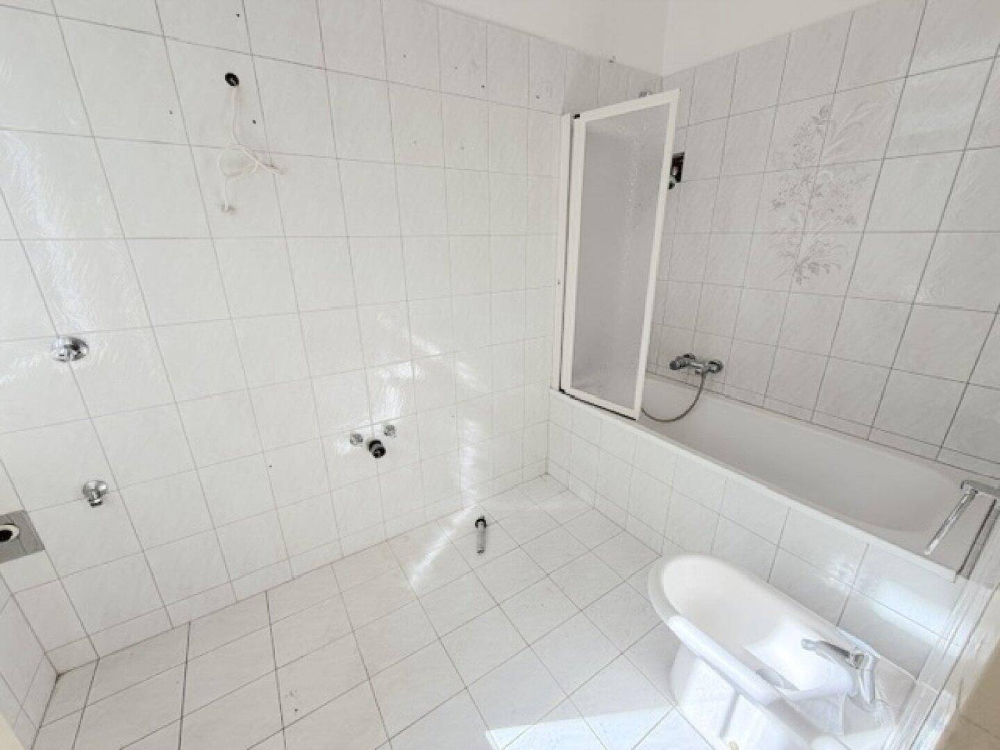 Badezimmer mit weißen Fliesen, Badewanne und Duschabtrennung, bereit zur Modernisierung.