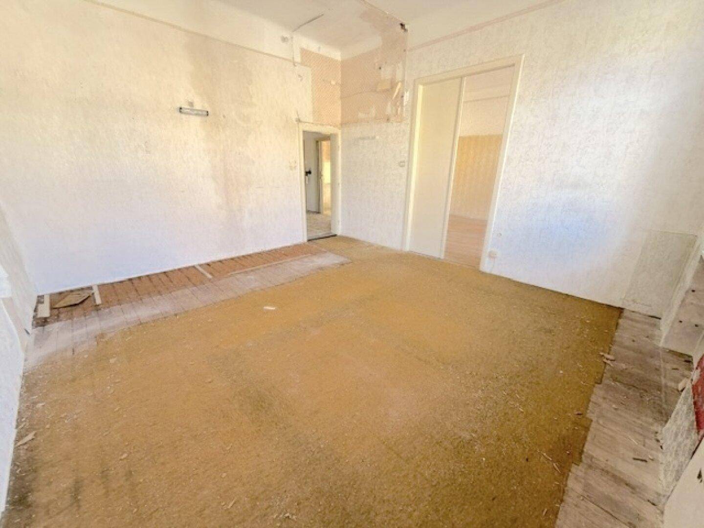 Geräumiges Zimmer mit altem Holzboden und freigelegten Wänden, bereit zur Sanierung.