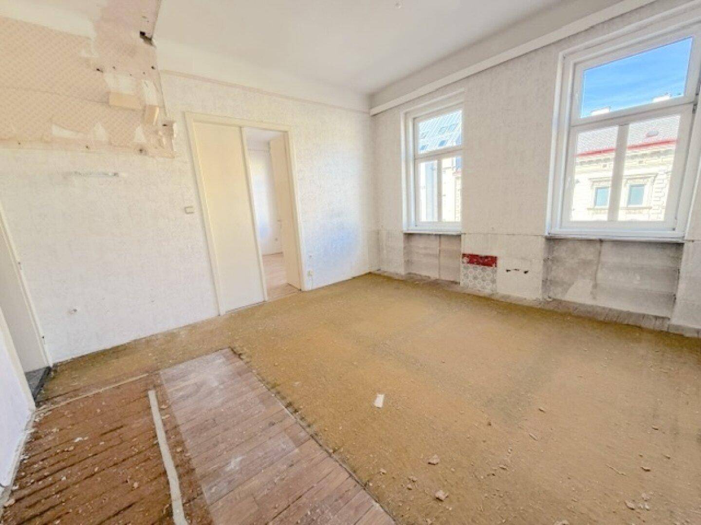 Renovierungsbedürftiges Zimmer mit freigelegten Wänden und altem Holzboden.