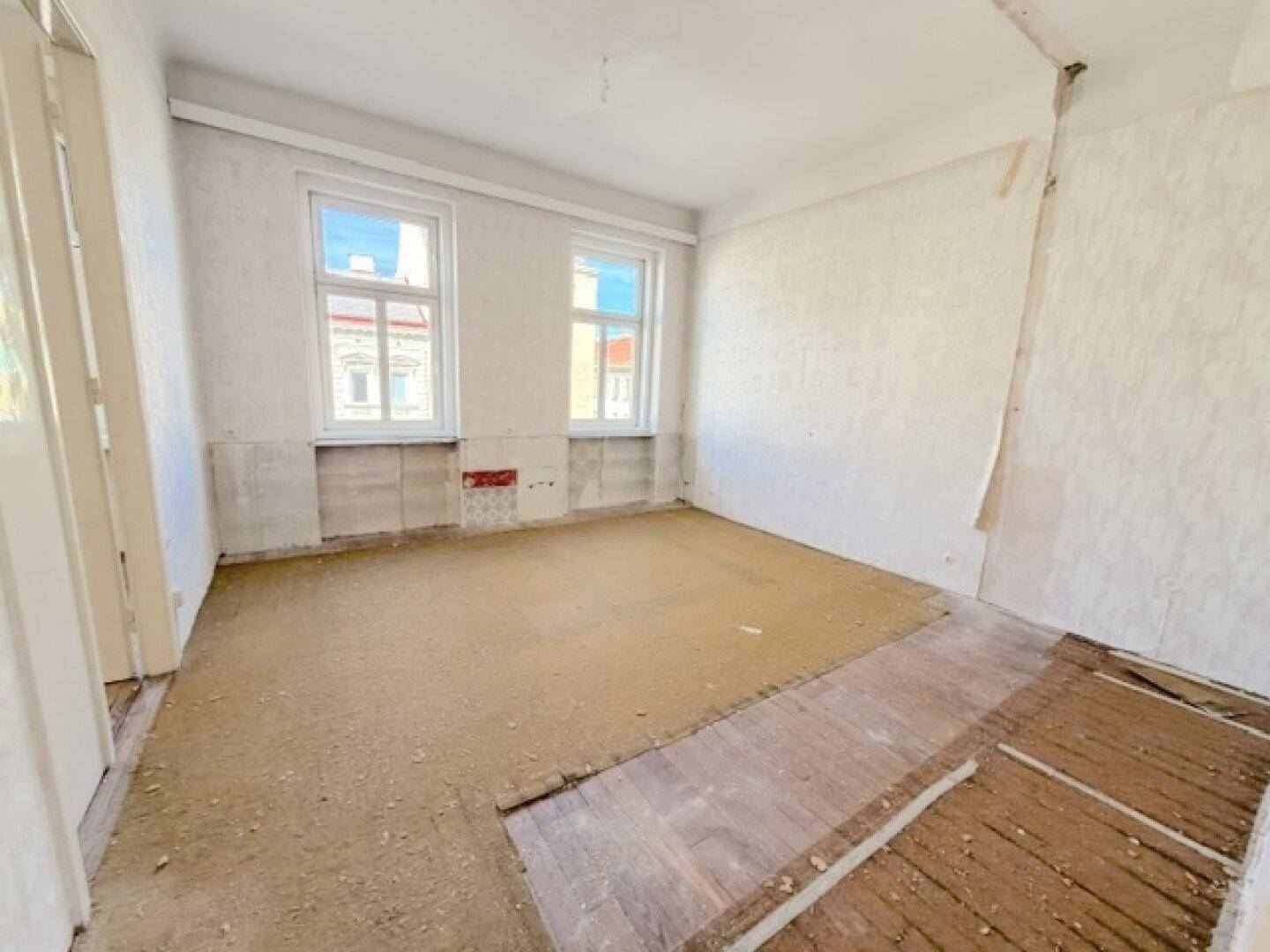 Renovierungsbedürftiges Zimmer mit freigelegten Wänden und altem Holzboden.