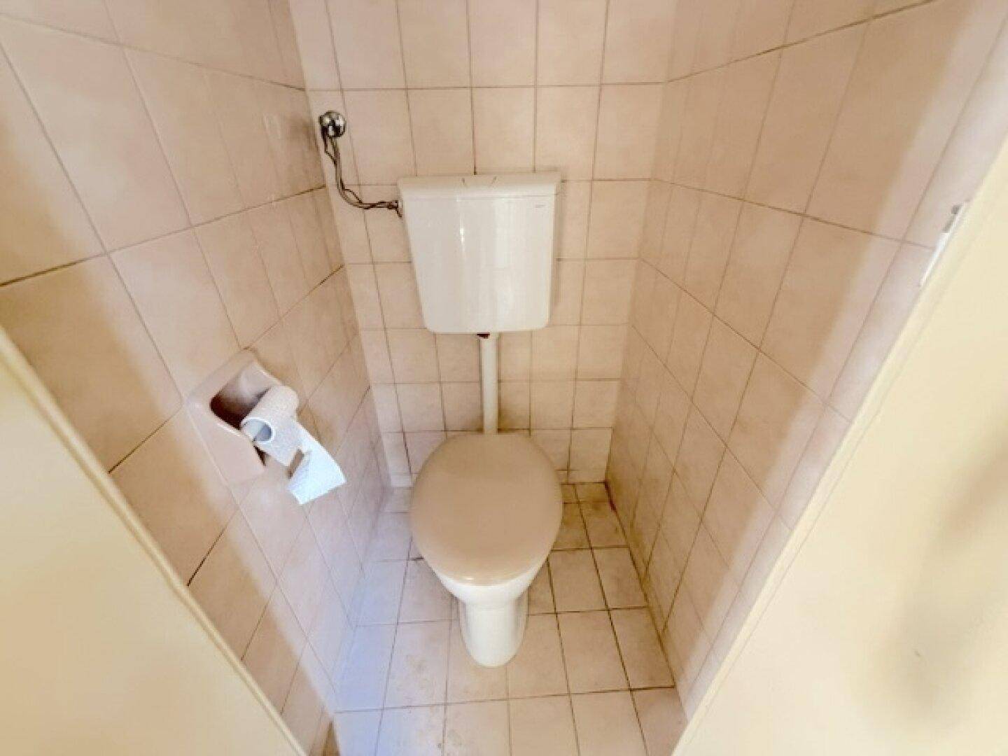 Kleines WC mit beigen Fliesen und traditioneller Toilette, renovierungsbedürftig.