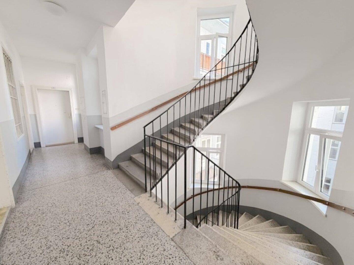 Repräsentatives Treppenhaus mit Terrazzoboden und schmiedeeisernem Geländer in einem Altbau.
