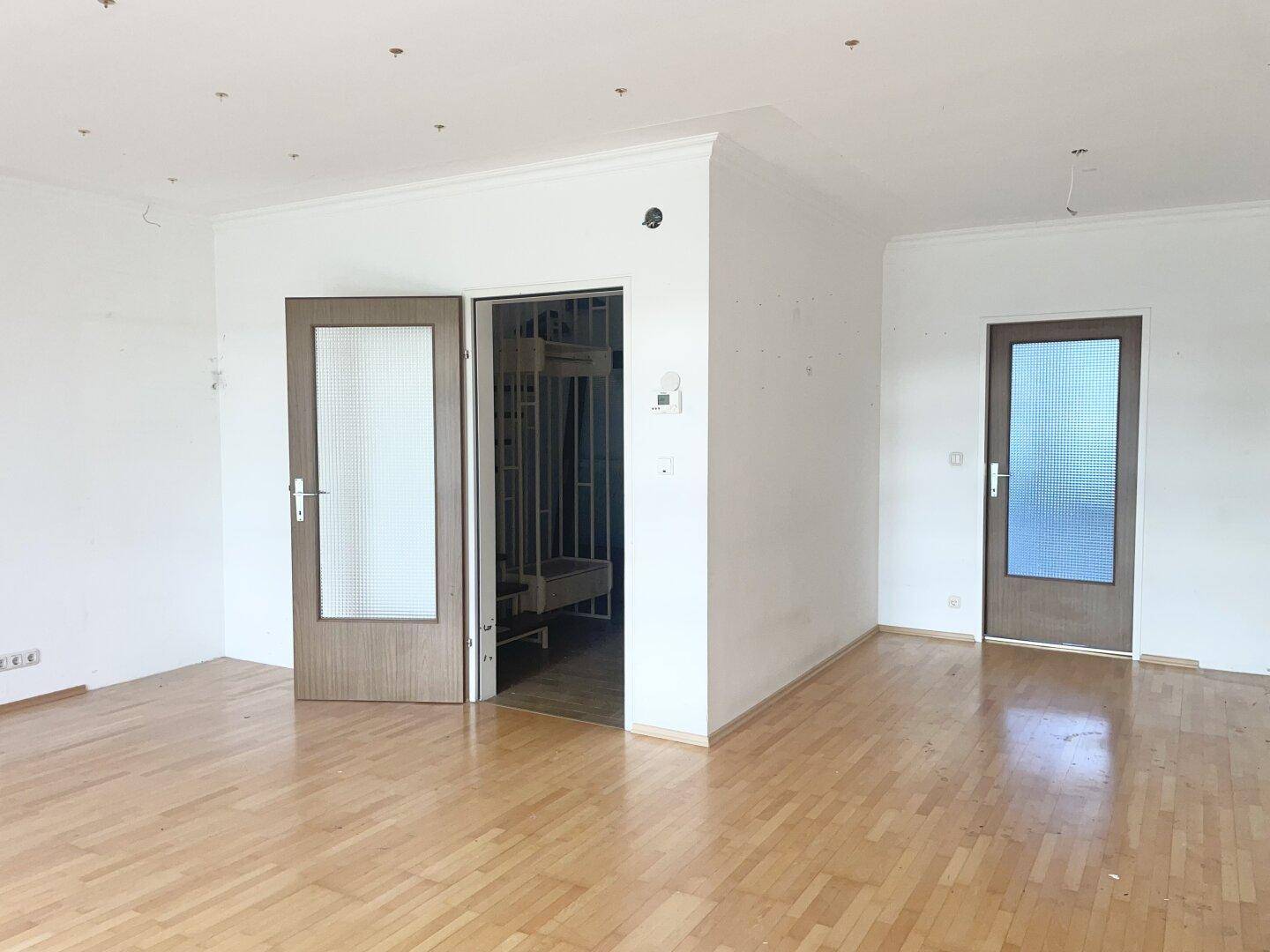 Geräumiges Wohnzimmer mit Parkettboden und zwei Türen, bereit zur individuellen Gestaltung.