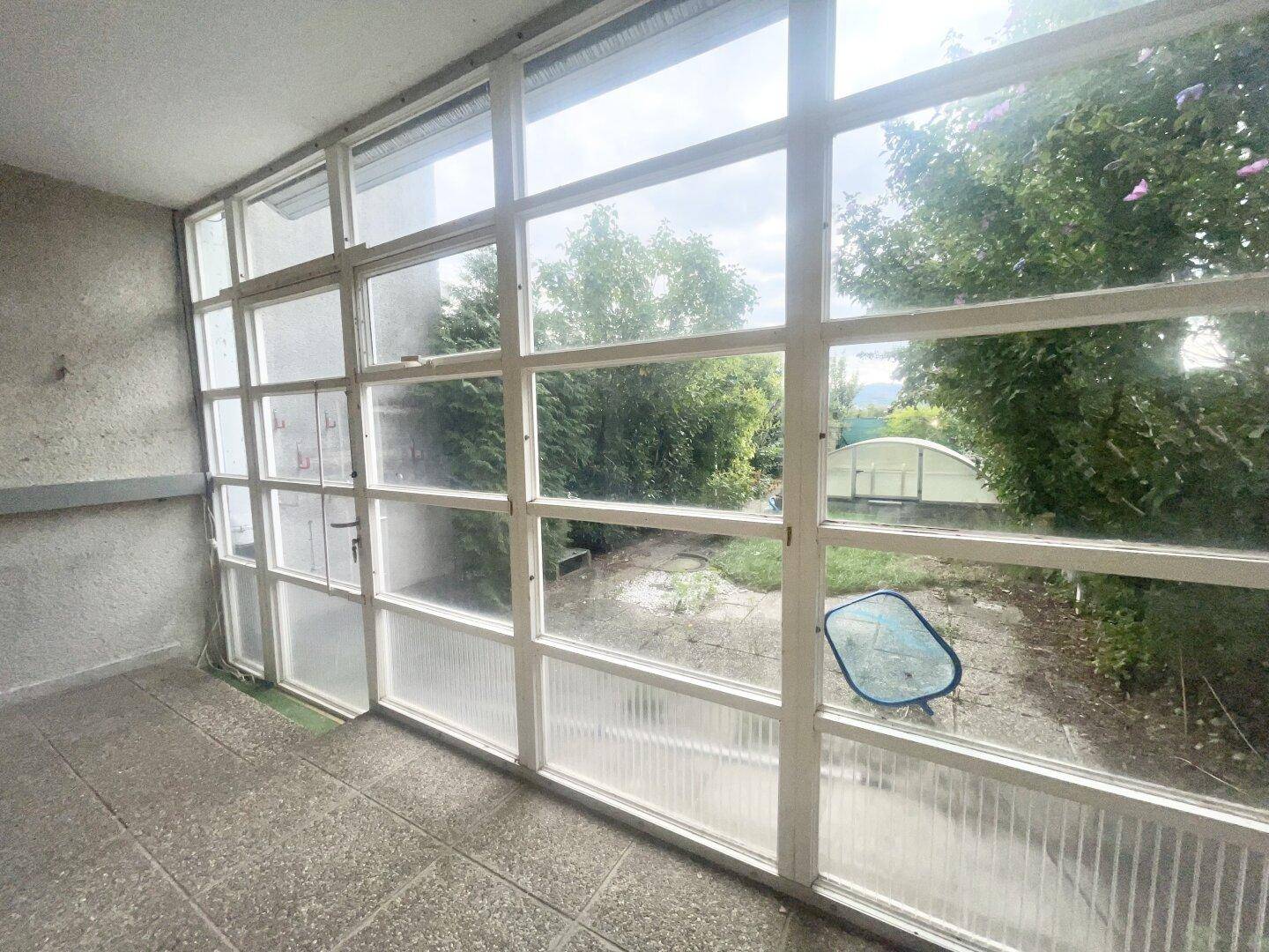 Verglaster Wintergarten oder Loggia mit Blick auf den Garten und den überdachten Pool.