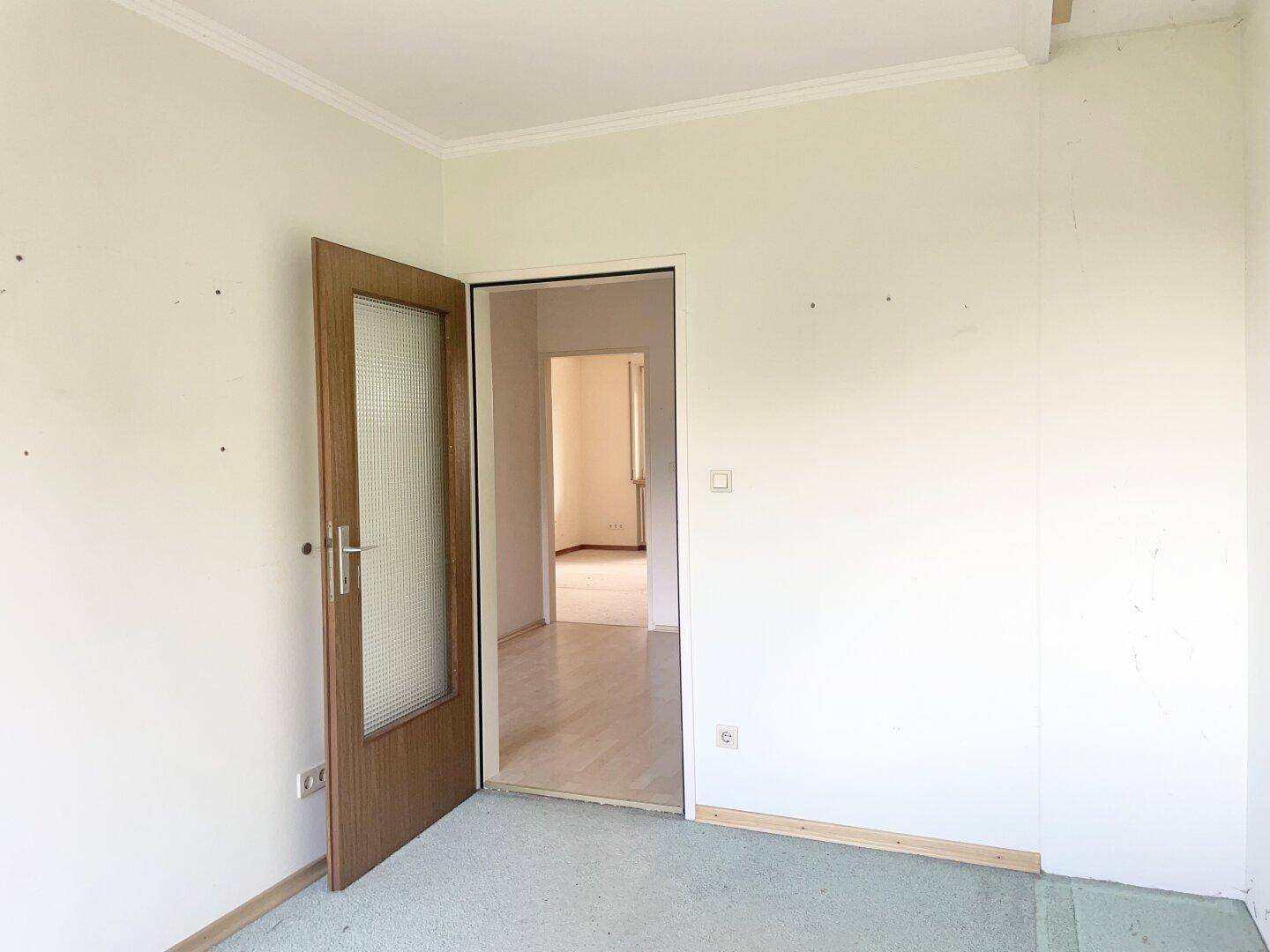 Schlafzimmer mit grünem Teppichboden und einer Tür, die den Zugang zu einem weiteren Raum ermöglicht.