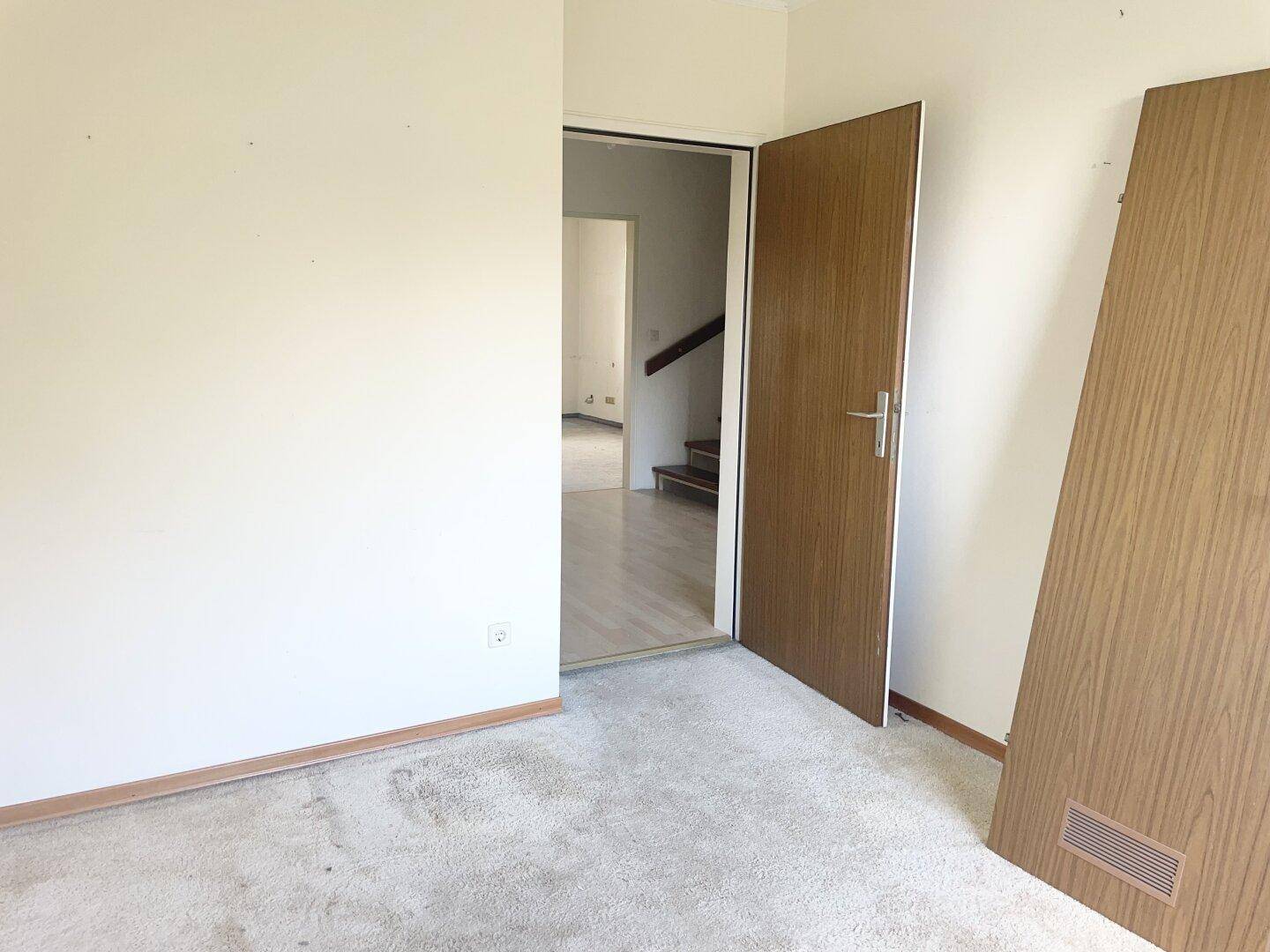 Schlafzimmer mit hellem Teppichboden und einer Tür, die in den Flur führt.