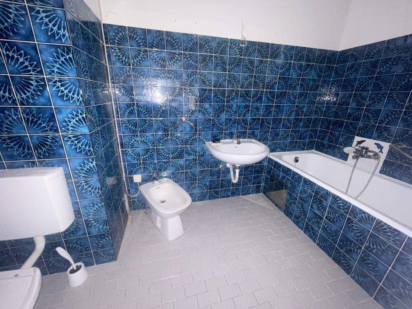 Badezimmer mit blauen gemusterten Fliesen, WC, Bidet, Waschbecken und Badewanne.