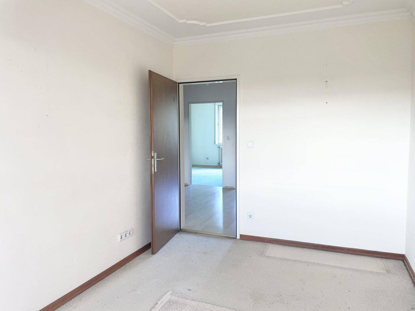 Schlafzimmer mit hellem Teppichboden und einer Tür, die den Raum mit dem Rest der Wohnung verbindet.