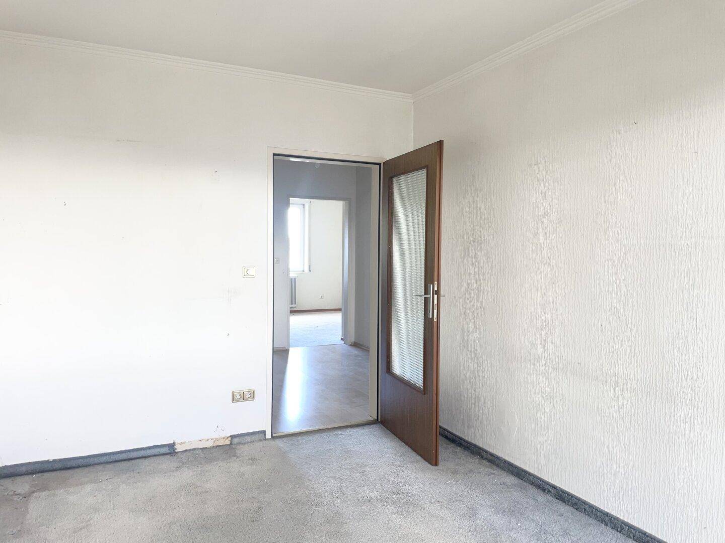 Schlafzimmer mit grauem Teppichboden und einer Tür, die zu einem weiteren Raum führt.