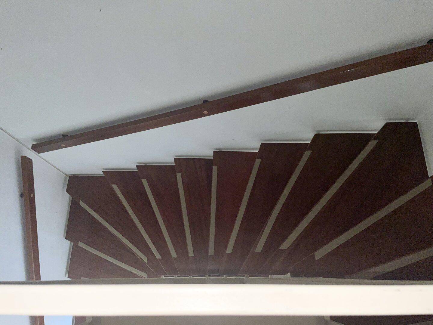 Dunkle Holztreppe mit schmalen Stufen, die in einem engen Treppenhaus nach oben führt.