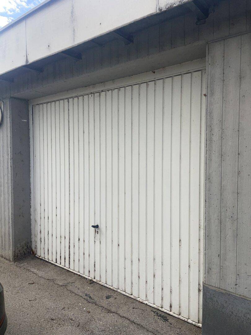Weiße Garagentür mit vertikalen Lamellen und sichtbaren Gebrauchsspuren an einer Betonwand.