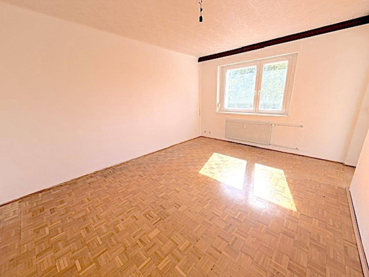 Leeres Zimmer mit Fischgrätparkett und viel Tageslicht durch das Fenster, bereit zur individuellen Gestaltung.