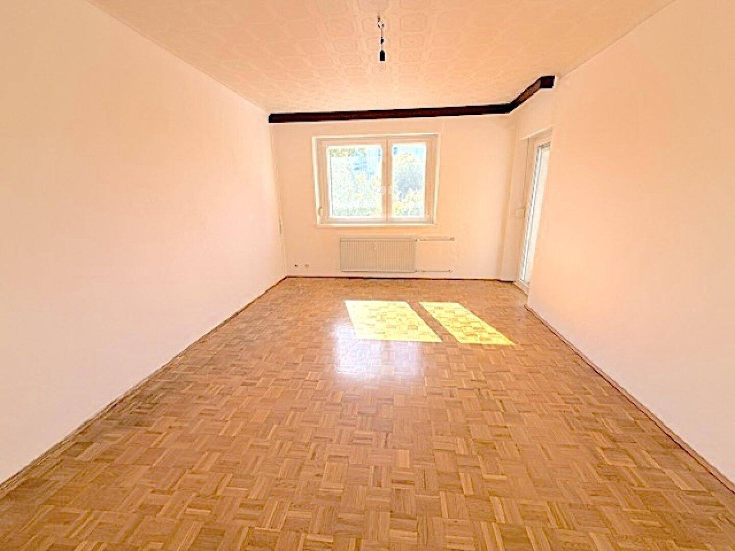 Heller Raum mit Parkettboden und großem Fenster, das viel Sonnenlicht hereinlässt, ideal für Wohnzwecke.