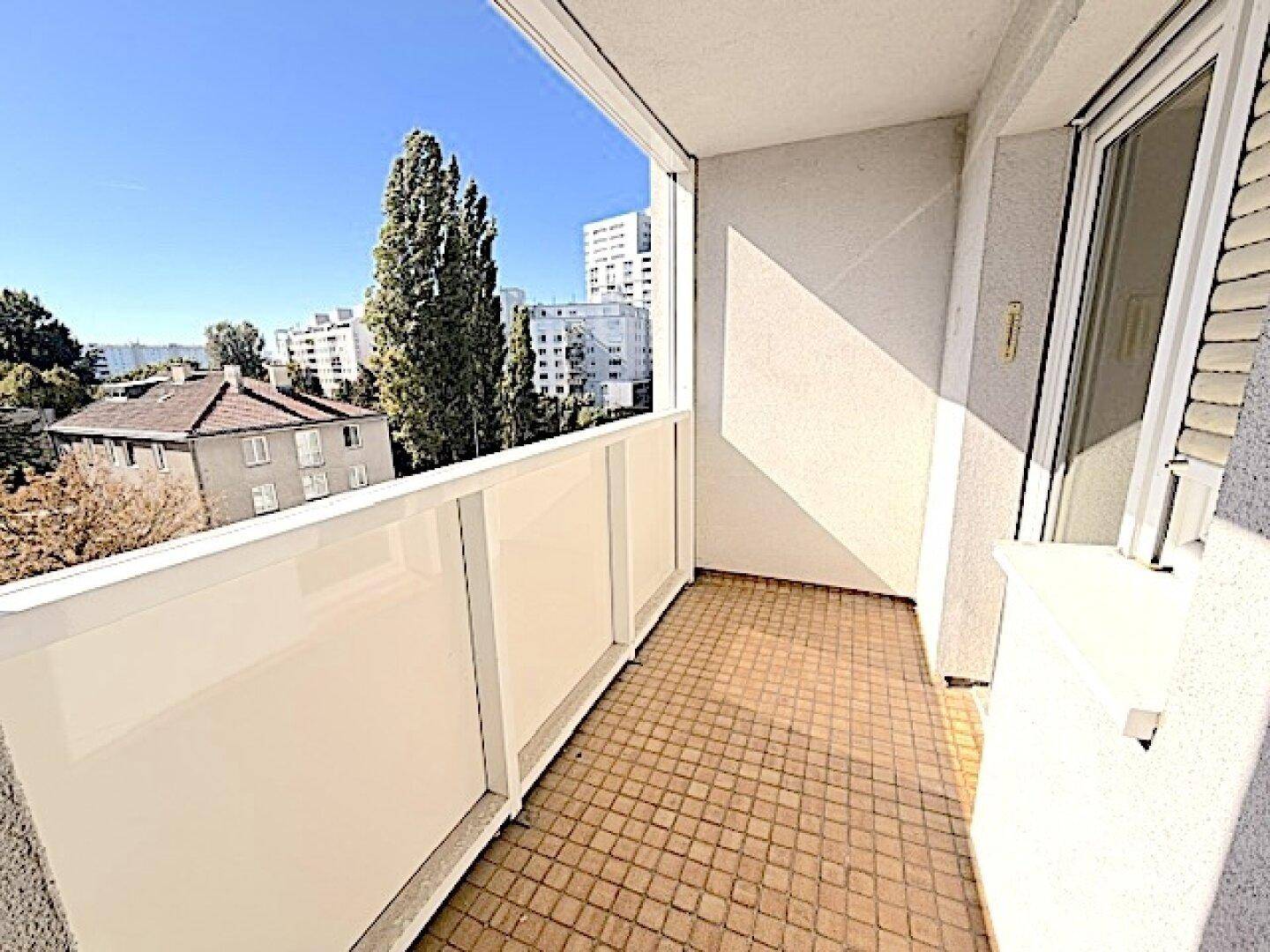 Sonniger Balkon mit Fliesenboden und weitem Blick über die Stadt und grüne Bäume.