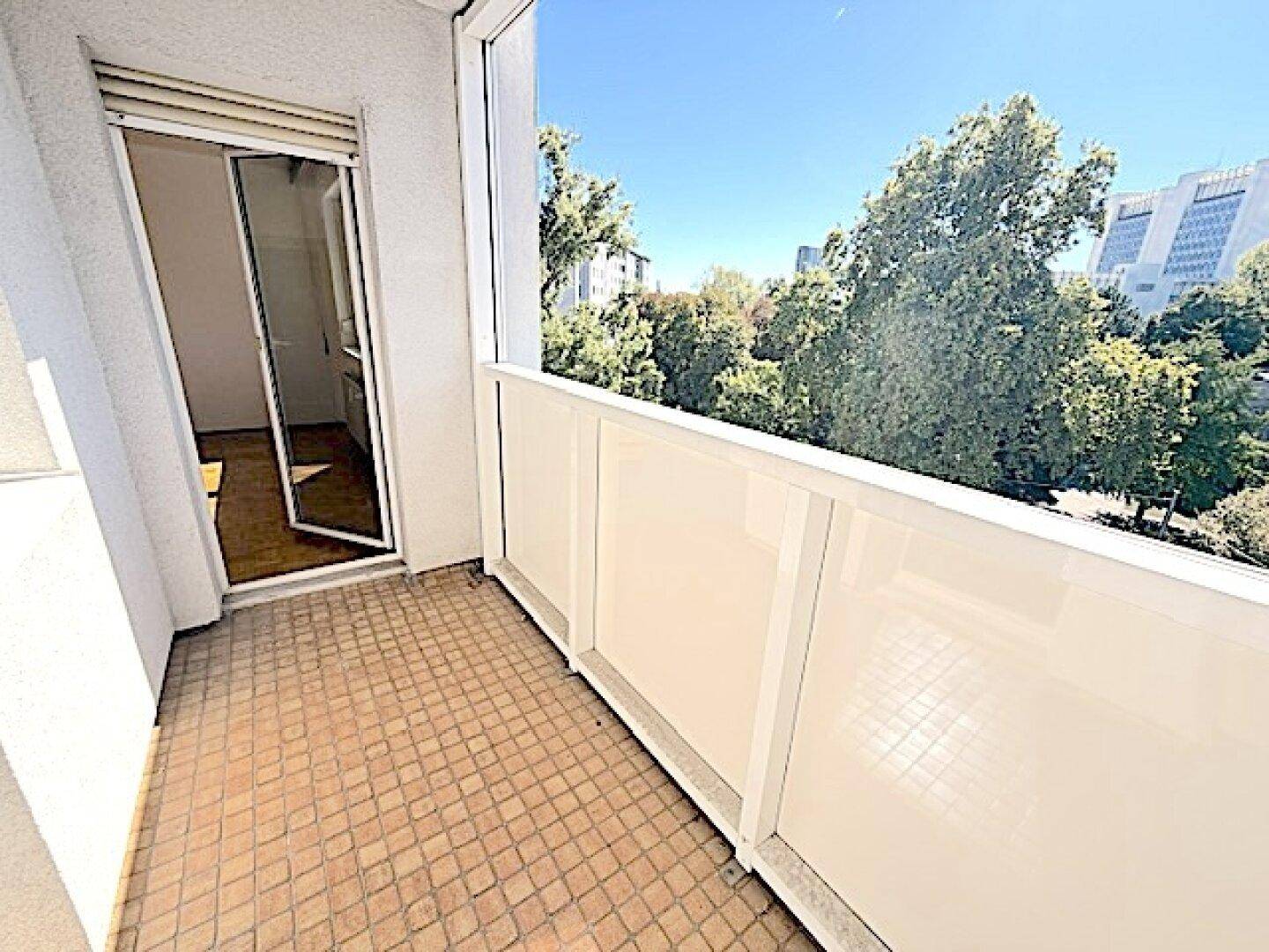 Balkon mit Fliesenboden und Blick auf die umliegenden Gebäude und grüne Bäume in der Ferne.