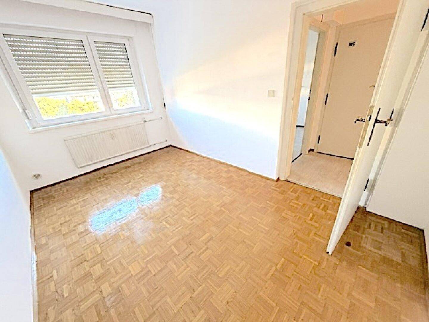 Heller Raum mit Parkettboden und Tür, die zu einem separaten WC führt, praktisch und gut aufgeteilt.