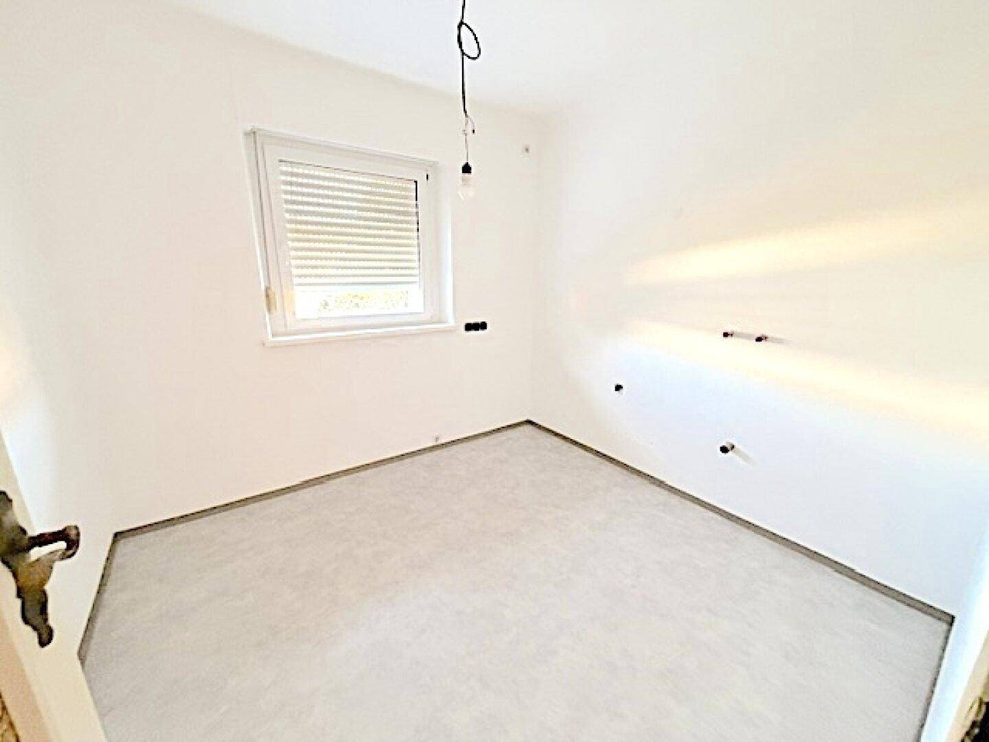 Leerer Raum mit Estrichboden und Fenster, vorbereitet für die Installation einer Küche oder eines Bades.